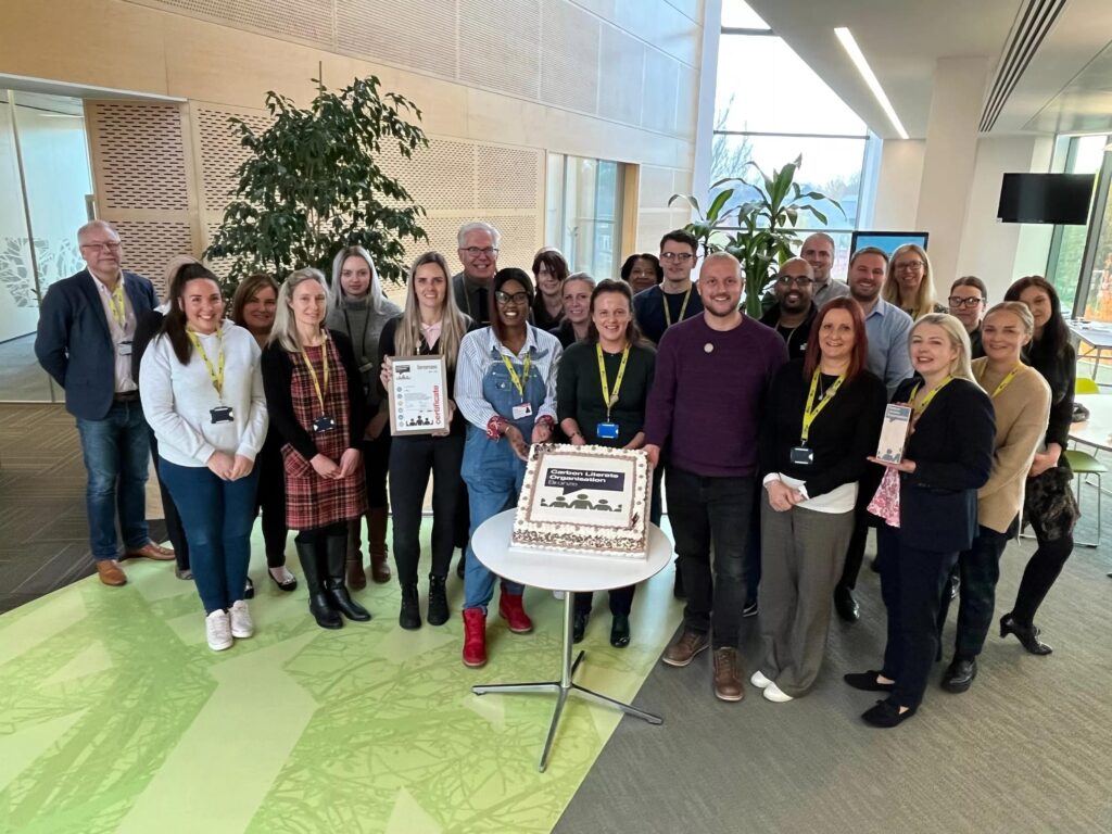 A group of colleagues standing around a cake which has a sustainability logo on it.